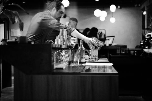 Free A monochrome image capturing a bartender arranging bottles behind a bar counter, creating a classic atmosphere. Stock Photo