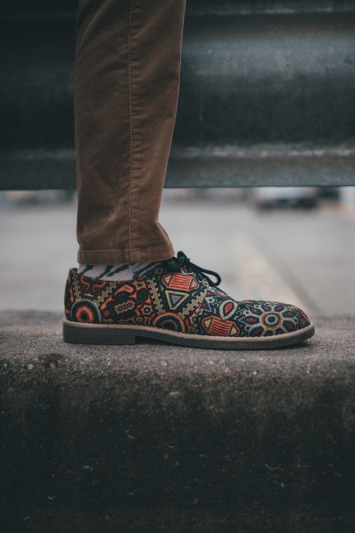Free Close-up of colorful patterned shoes paired with brown pants on a city sidewalk. Stock Photo