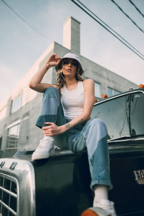 Free A stylish young woman in casual street fashion sits on a truck hood, showcasing urban youth culture. Stock Photo