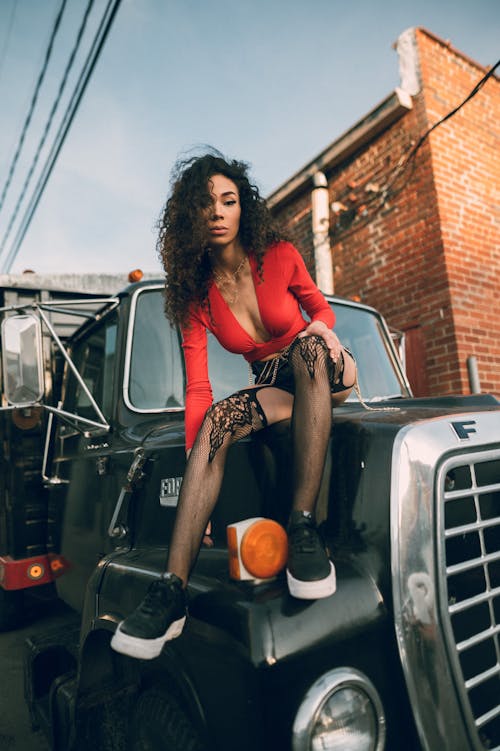 A Woman Wearing a Sexy Red Top Sitting on the Hood of a Truck