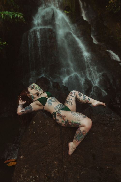 Free Tattooed woman in bikini lying on rocks near a mystical waterfall. Nature escape. Stock Photo