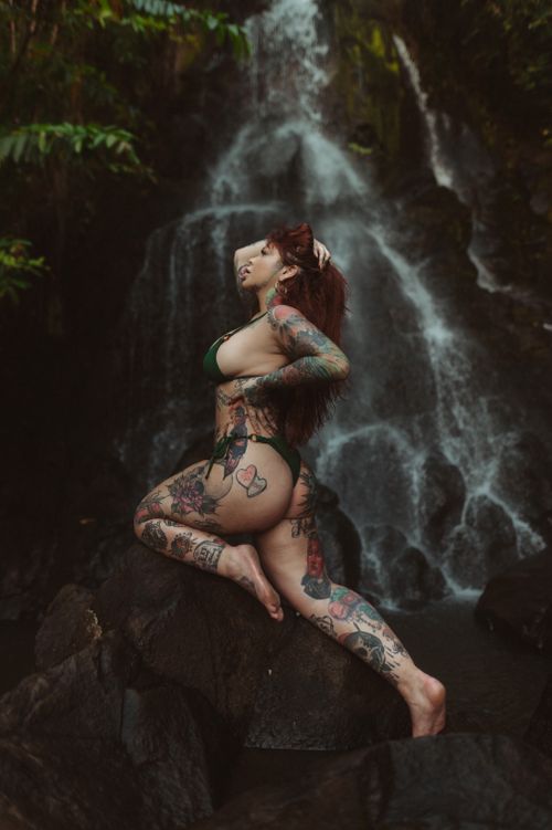 Free A tattooed woman in swimwear posing on rocks by a waterfall, showcasing vibrant body art. Stock Photo