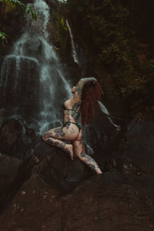 Free Tattooed woman posing on rocks by a waterfall, exuding natural beauty. Stock Photo