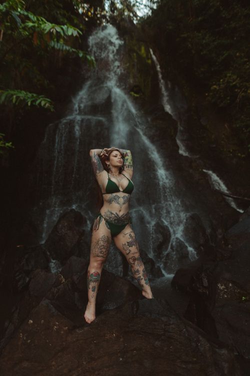 Free A tattooed woman in a bikini poses confidently by a waterfall, embracing nature's beauty. Stock Photo