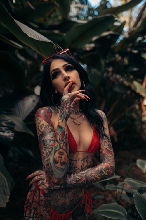 Free Woman with tattoos and red bikini in lush tropical setting, contemplating serenity. Stock Photo