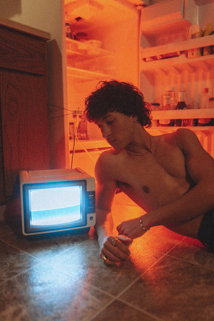 Man Lying On Floor Next To Open Fridge With Vintage TV