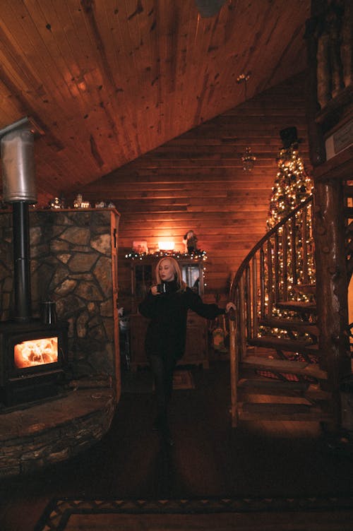 Woman in a Cosy Wooden Cabin with a Christmas Tree and a Fireplace 