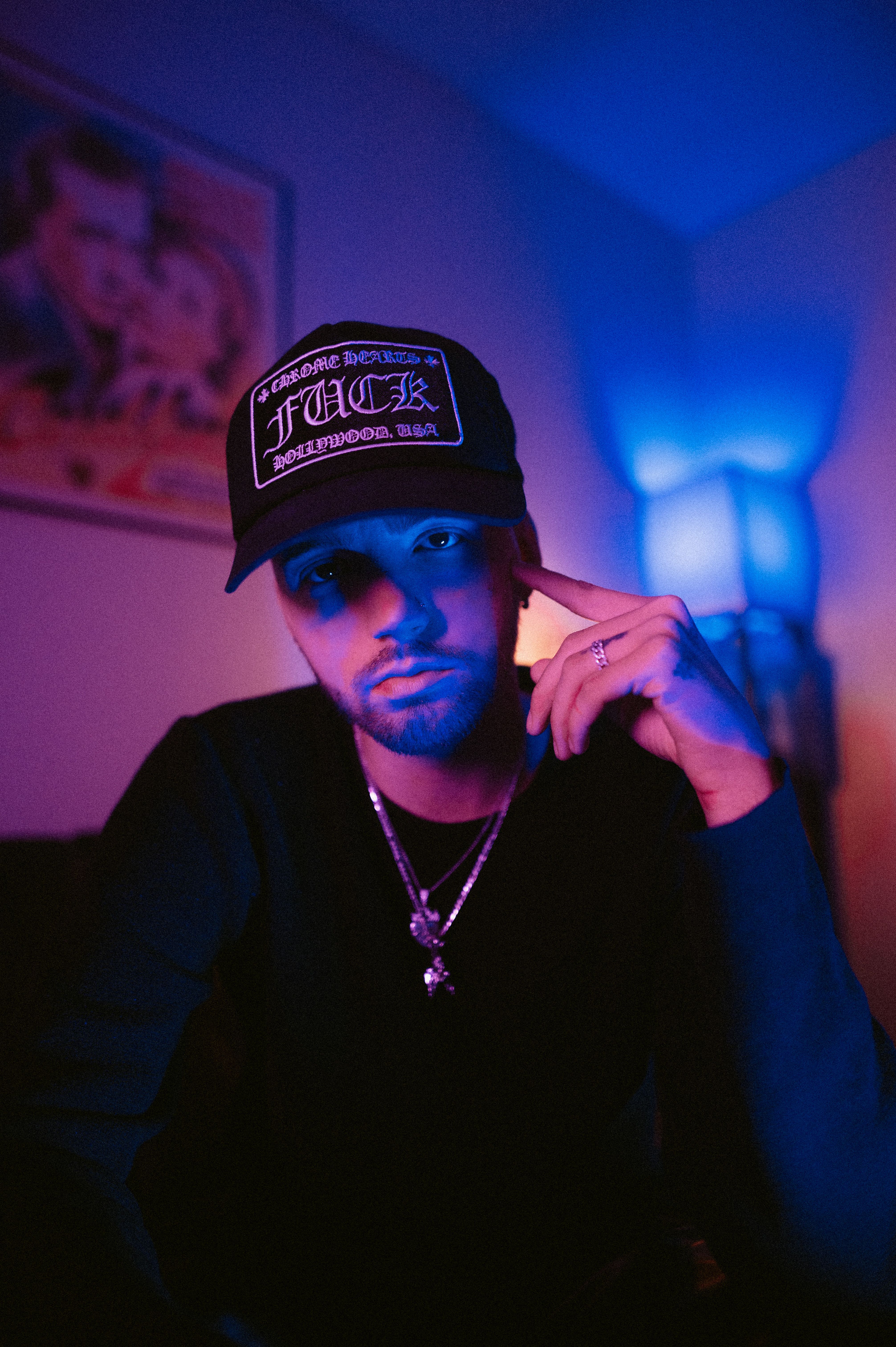 Dramatic portrait of a man indoors, wearing a cap and jewelry, illuminated by creative lighting.