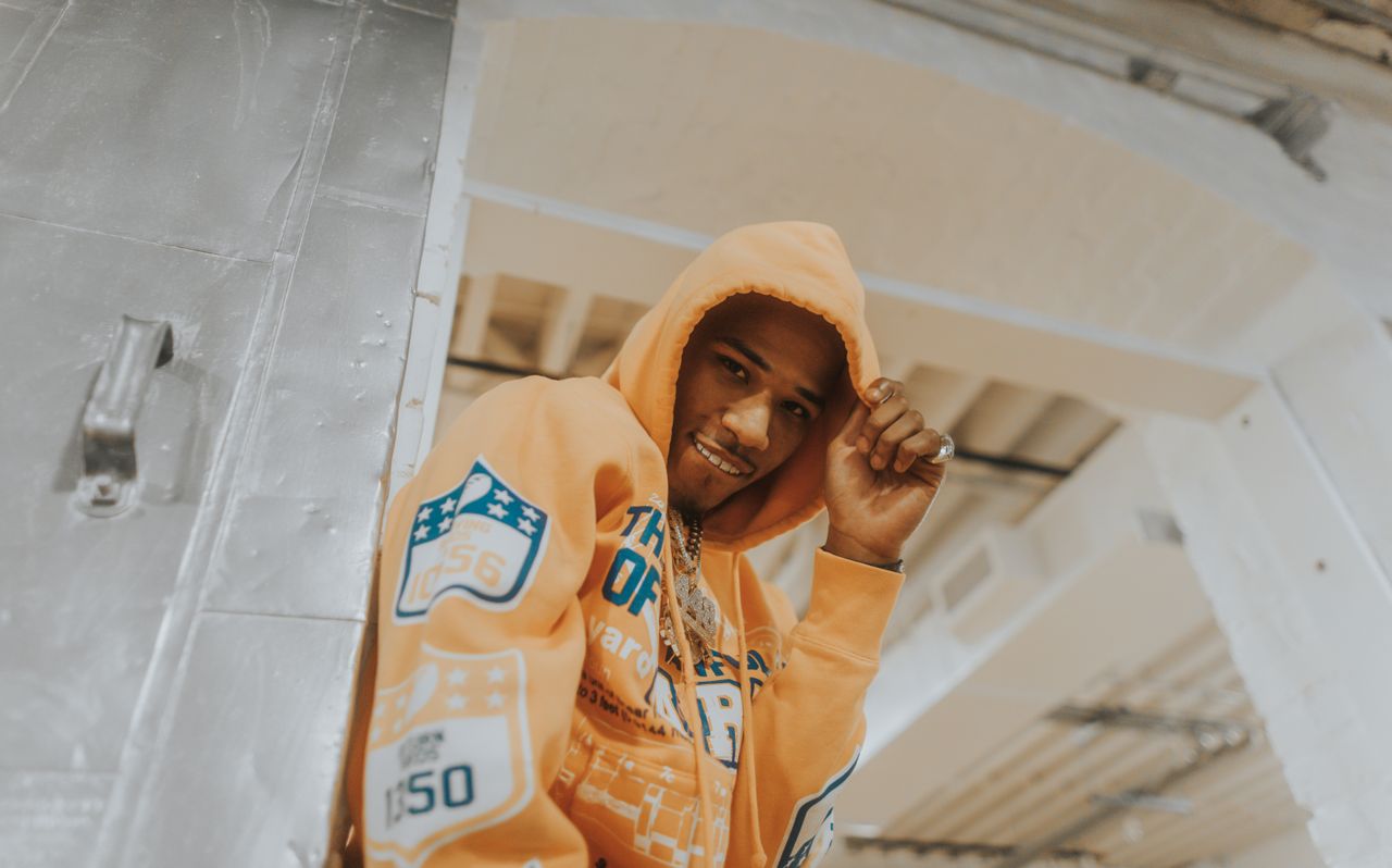 a smiling young man wearing a vibrant orange hoodie indoors creating a