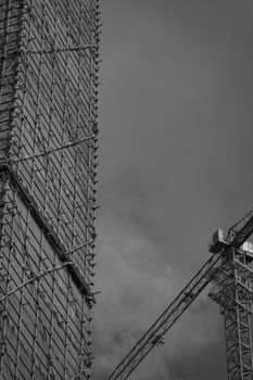 Black and white image of buildings under construction with cranes and a cloudy sky backdrop.