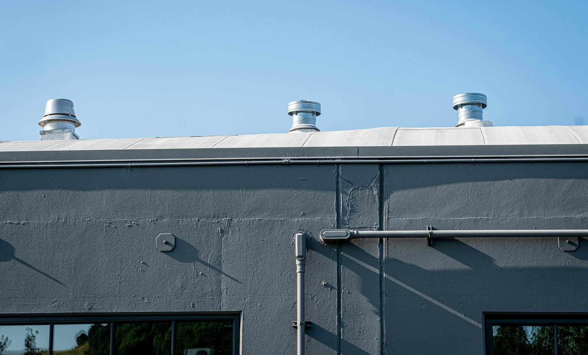 Exterior of a gray industrial building with rooftop vents under a clear blue sky.