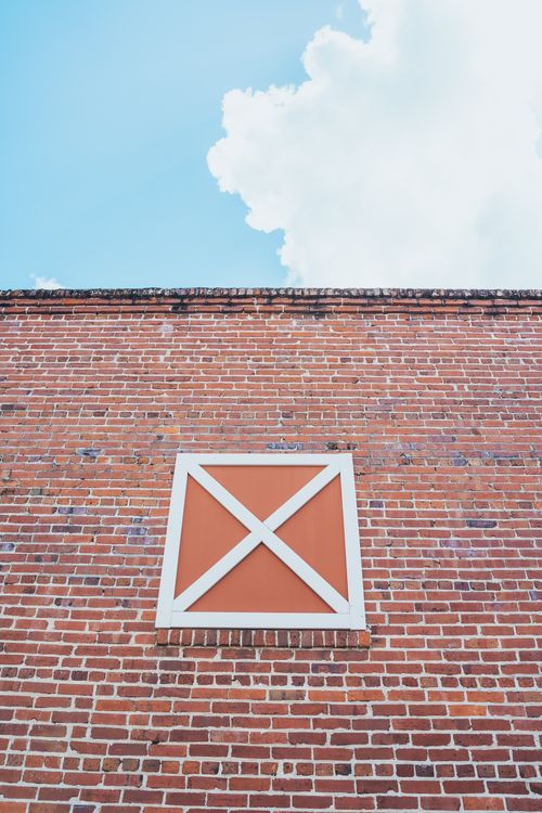 Free Low-angle view of a brick wall with a decorative wooden panel set against a blue sky with clouds. Stock Photo
