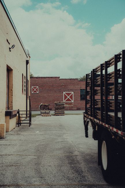 A transport truck in an industrial warehouse yard with pallets and brick buildings.