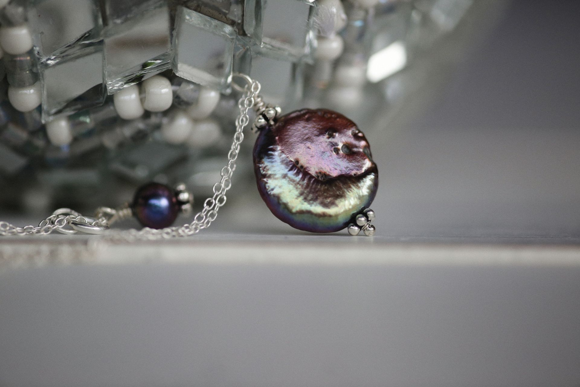 Close-up of a luxurious pearl necklace with silver chain on a reflective surface, perfect for elegant fashion.