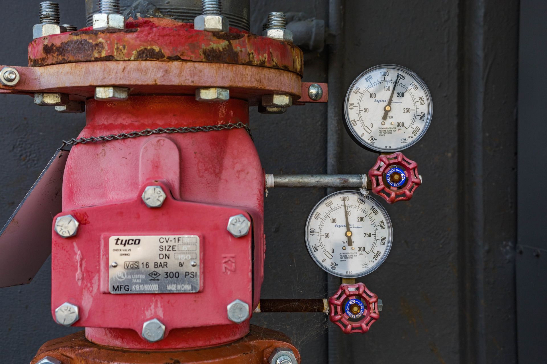 Close-up of industrial pressure gauge and valve mechanism with red paint and rust.