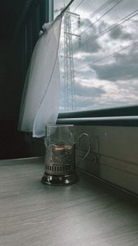Warm tea glass on train's windowsill with view of cloudy sky and power tower.