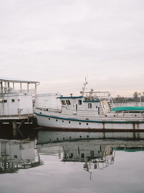 Free A fishing boat docked at a tranquil harbor pier under a cloudy sky. Stock Photo