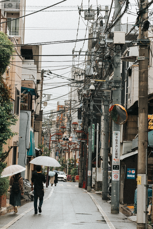 Free Two people walking on a rainy urban street with umbrellas in a busy neighborhood. Stock Photo
