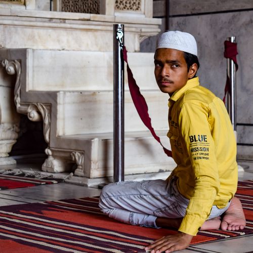 Free Young man wearing a yellow shirt kneels on a patterned rug indoors, looking over his shoulder. Stock Photo