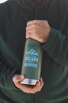 一名穿着休闲装的男子拿着一个写着西班牙语的绿色保温水瓶