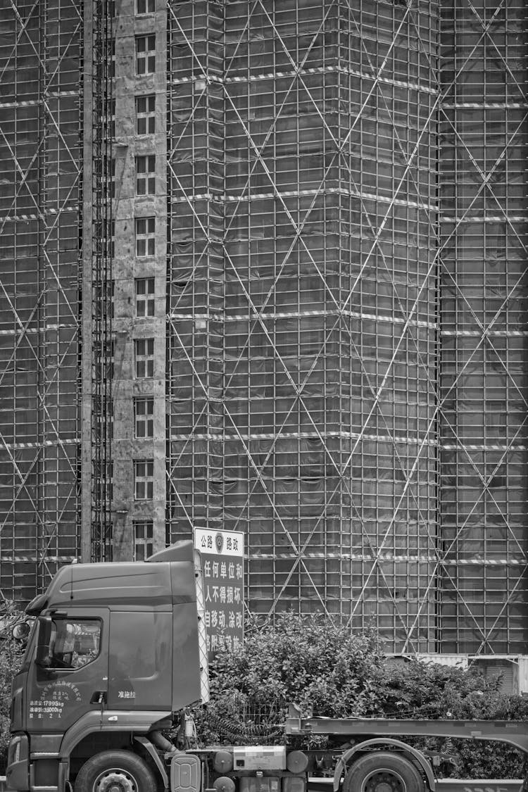 Grayscale Photo Of A Truck Passing A Building Under Construction