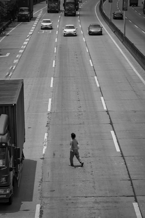 Grayscale Photo of a Kid Walking in the Middle of a Road