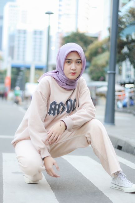 Fashionable young woman in hijab crouching on urban street, showcasing modern style.
