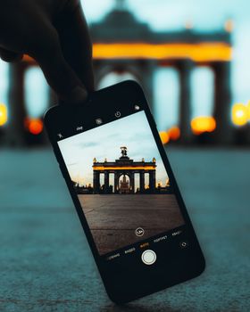 Close-up of a smartphone capturing Moscow's famous Triumph Arch at dusk.