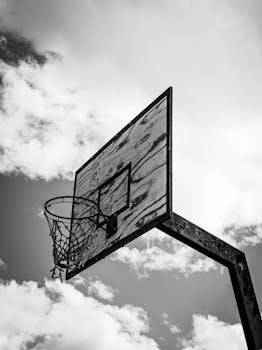 Monochrome shot of a rustic basketball hoop against a cloudy sky, emphasizing contrast.