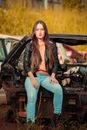 A Woman in Black Leather Jacket Sitting on a Junk Car