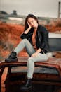 Woman in Black Leather Jacket and Gray Denim Jeans Sitting on Brown Wooden Bench