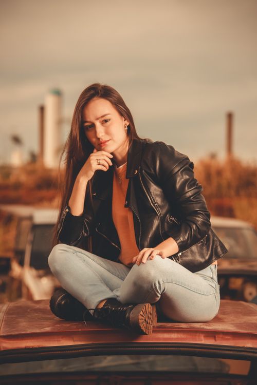 Free Fashionable woman in leather jacket posing on a car roof surrounded by an industrial setting. Stock Photo