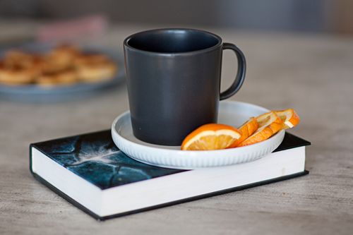 Free Black mug on a saucer with orange slices, placed on a book for a cozy morning vibe. Stock Photo