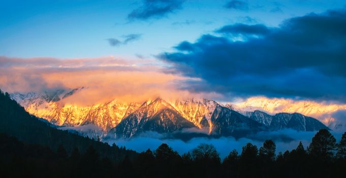 Majestic snow-covered mountains at twilight with vibrant sky and dramatic clouds, captured in Tibet's breathtaking landscape.