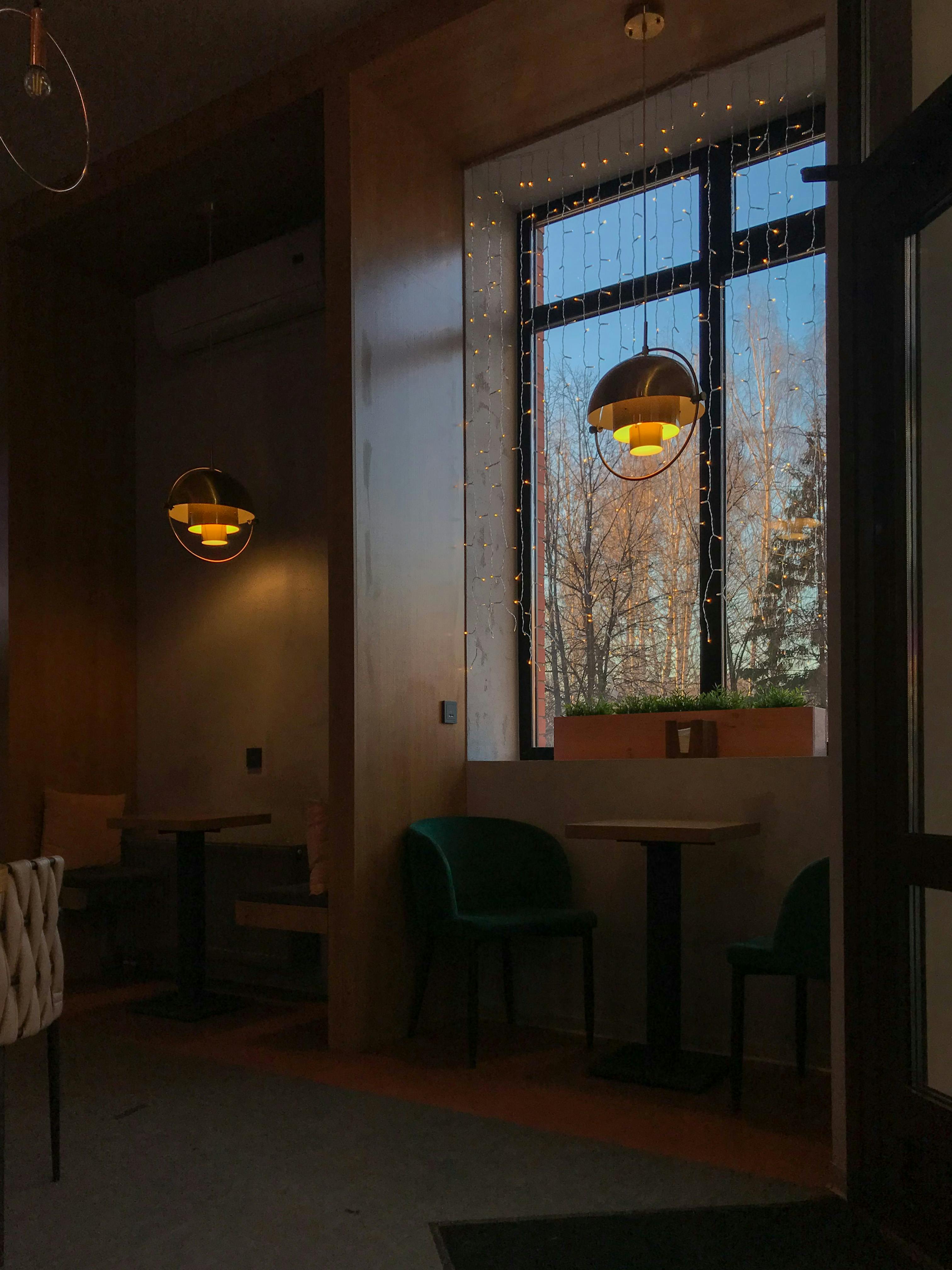 Free Warm and inviting café interior featuring modern furniture and elegant lighting with a view outside. Stock Photo