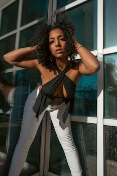 Fashionable woman posing by a modern glass building, showcasing bold style and confidence.