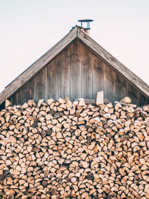 Free A rustic wooden shed with a neatly stacked pile of firewood against a clear sky. Stock Photo