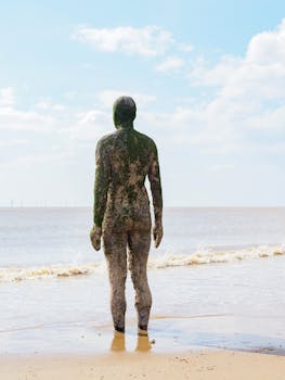 Mossy statue on a seaside beach in the UK, under a bright sky.