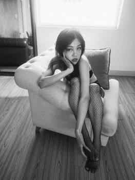 Artistic black and white portrait of a young woman posing on a chair indoors.