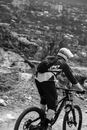 Grayscale Photo of Man in Black Jacket and Pants With Helmet Riding on Mountain Bike