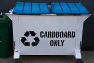 A white recycling container marked "Cardboard Only", featuring a blue lid and recycling symbol.