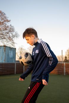 A teenage boy skillfully plays soccer outdoors in Støvring, Denmark, during the day.