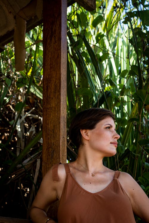 Close-Up Shot of a Woman in Brown Sleeveless Shirt Leaning on Wooden Post

