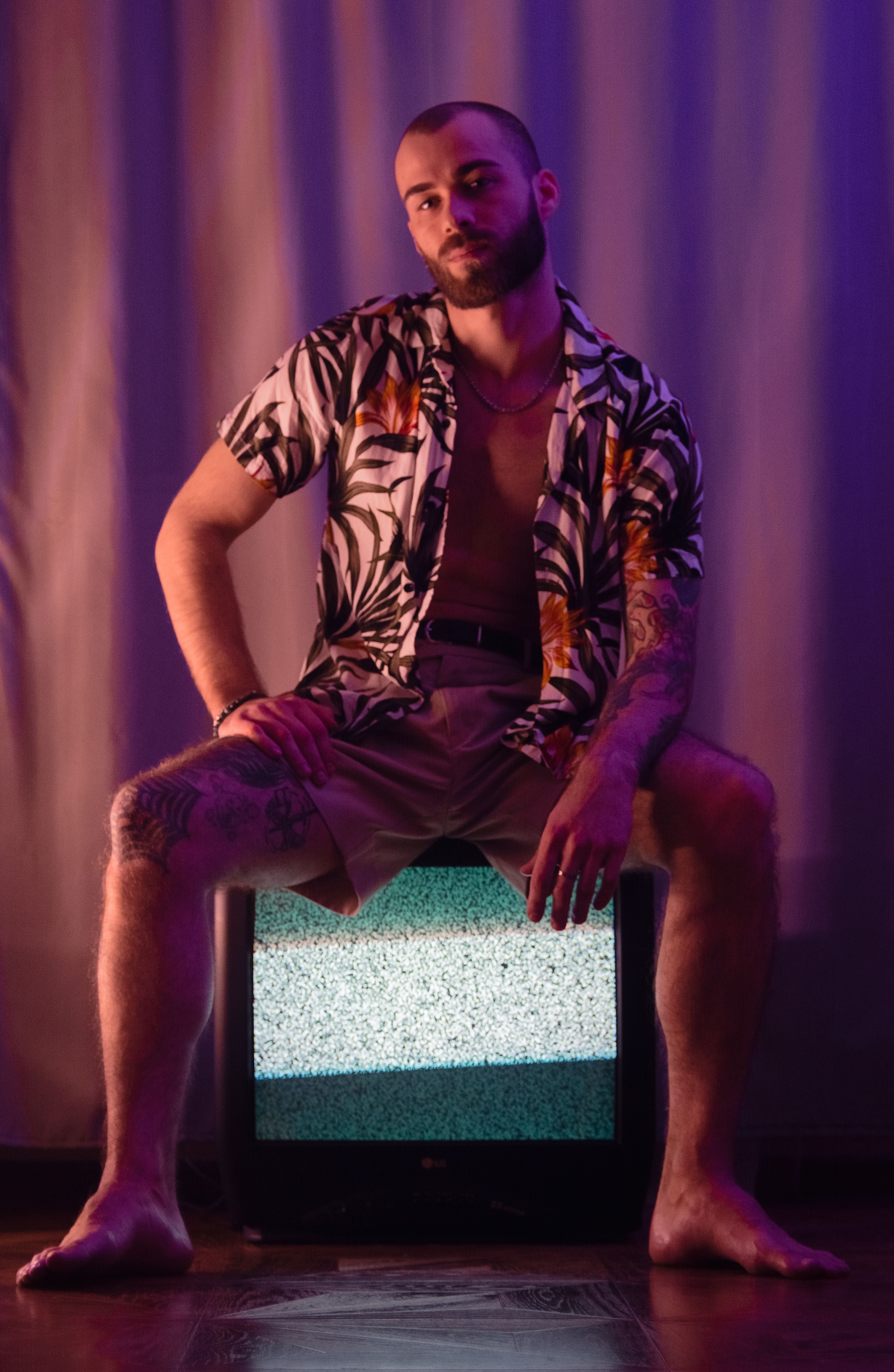 Fotomural Retrato de un hombre tatuado posando con un estilo retro en un televisor vintage en interiores.