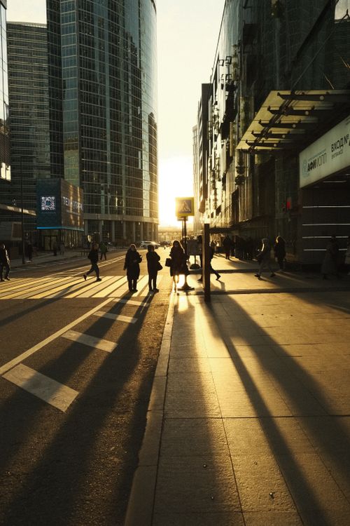 Free Silhouetted pedestrians walking during sunset in Moscow's urban cityscape with tall buildings casting long shadows. Stock Photo