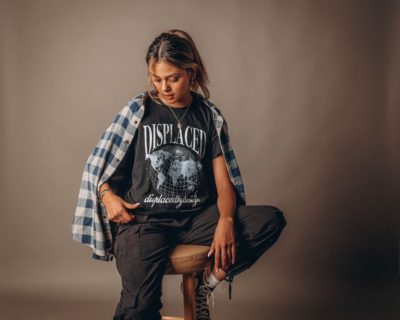 Young woman sitting on a stool in trendy streetwear during a studio shoot.