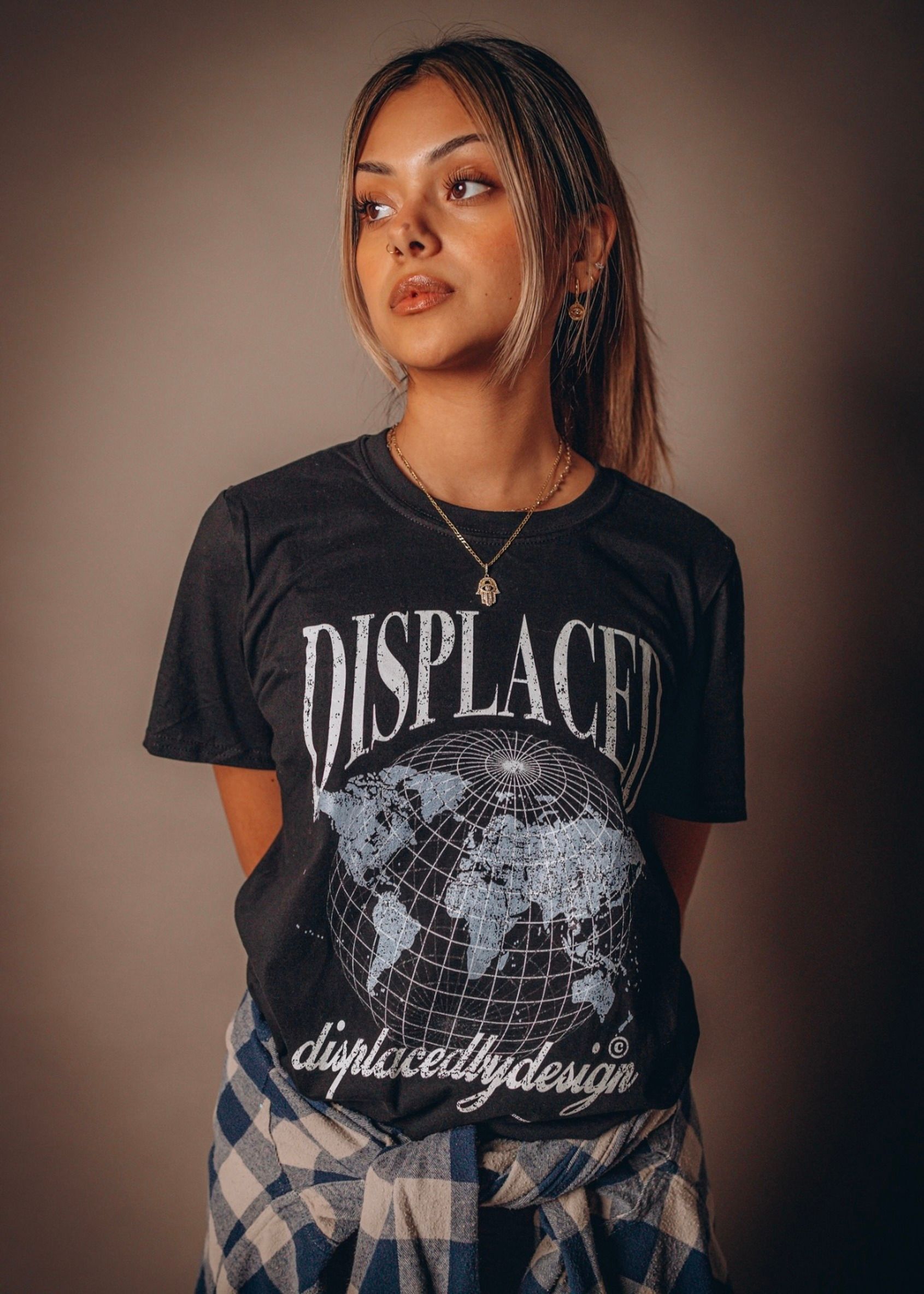 Side profile of a young woman in a studio wearing a 'Displaced' t-shirt, looking thoughtfully away.