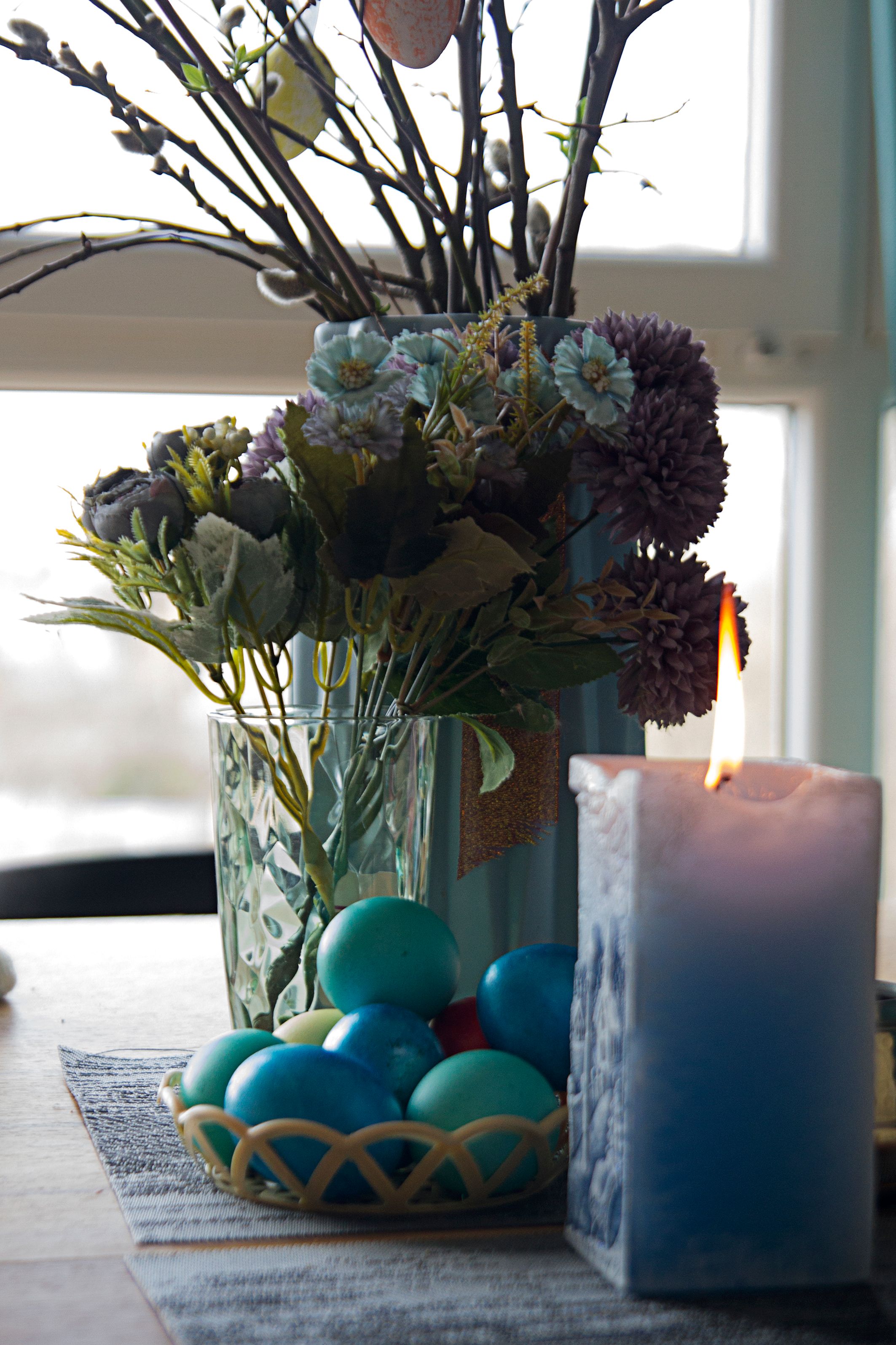 Vibrant Easter-themed arrangement with colored eggs, flowers, and a candle.