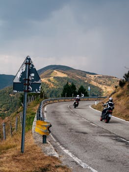 Two motorcyclists navigate a winding mountain road under a moody sky, ideal for adventure themes.