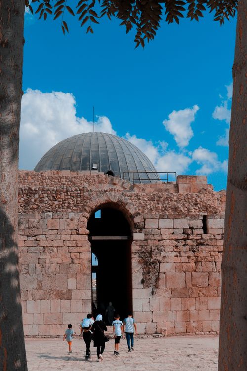 Free Visitors exploring the ancient Umayyad Palace in Amman with its iconic dome under a clear blue sky. Stock Photo
